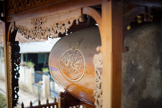 Close-up of traditional Bedug drum featuring beautiful Arabic calligraphy on its wooden body, framed by intricate hand-carved wooden pavilion details