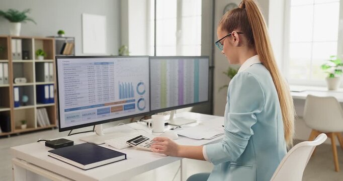 Analyst businesswoman reviews finance data reporting dashboard. She works at dual monitors reviewing charts, spreadsheets, and graphs for budgeting. Clear data analysis and financial reporting