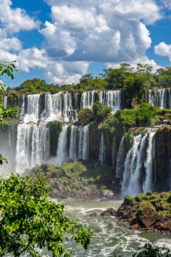 Majestic Iguazu Falls in Iguazu National Park, cascading water and lush green rainforest under a blue cloudy sky, natural wonder of the world