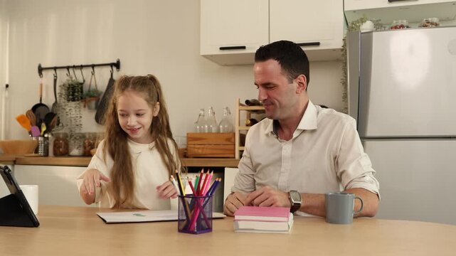 A father and daughter giving each other a high five while sitting at a kitchen table with colored pencils and books.
