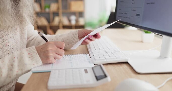 Senior woman notes electricity bill payment at home. On the computer with calculator and notebook she tracks expenses and finance, updates logs and plans budgeting. Home money theme in focus.