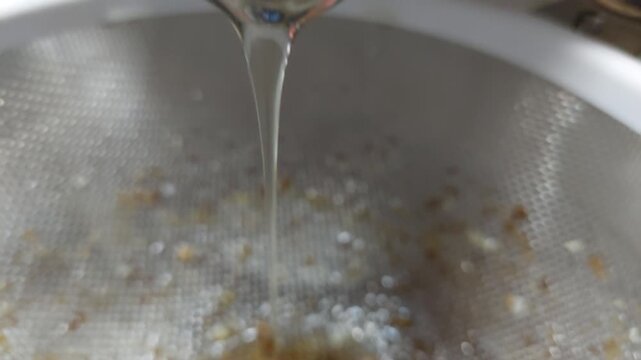 Macro shot of raw organic honey pouring through a metal sieve strainer