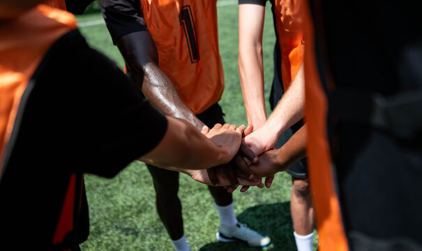 Soccer players stacking hands together in a team huddle before a match, demonstrating unity