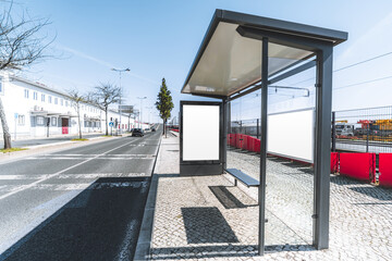Naklejka premium Two blank advertising display mockups at a modern glass bus shelter beside a sunny urban road, with clear copy space on the left for design presentation