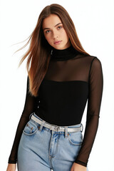 Fototapeta premium Young woman with long brown hair wears black mesh top and blue jeans. She stands against plain white background, looking directly at camera with gentle expression. Her hair blows slightly to side.