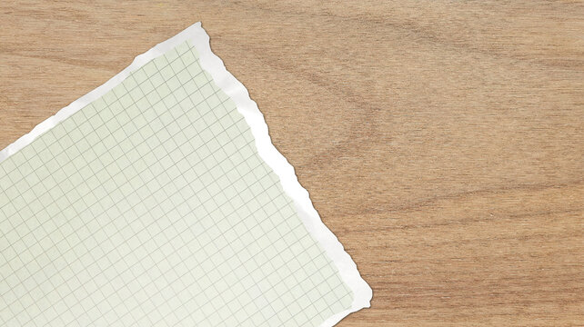 Torn sheet of green grid notebook paper on light brown wood grain texture background, ripped piece of math graph blank notepad page with copy space for text note message flat lay mockup template.