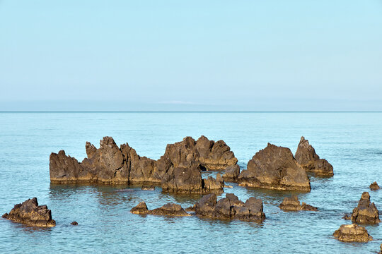 Sharp volcanic rocks in the calm Mediterranean sea under a clear blue sky in Scalea, Calabria, Italy. Beautiful coastal marine landscape.