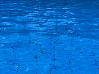 Naklejka premium Wavy blue water surface in a swimming pool with submerged mosaic tiles background.