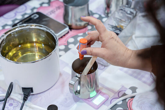 Person adding color to melted wax during candle making workshop