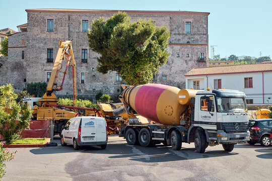 Concrete mixer truck and pump working on a construction site in Italy. Industrial machinery next to a historic stone building in Scalea, Calabria.