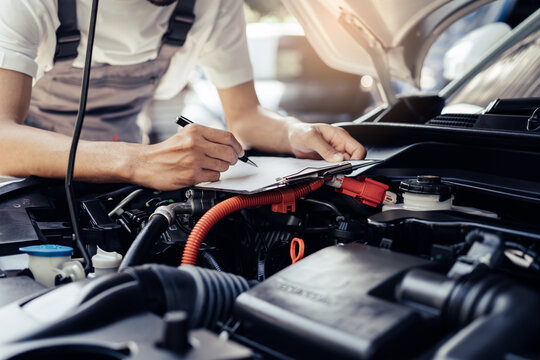 Auto check up and car service shop concept. Mechanic writing job checklist to clipboard to estimate repair quotation to client at workshop garage.