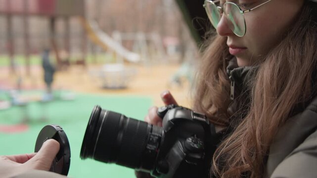 Asian woman adjusting DSLR settings, checking viewfinder and turning dials, testing exposure and focus, closeup hands on camera, patient concentration and careful technique in park