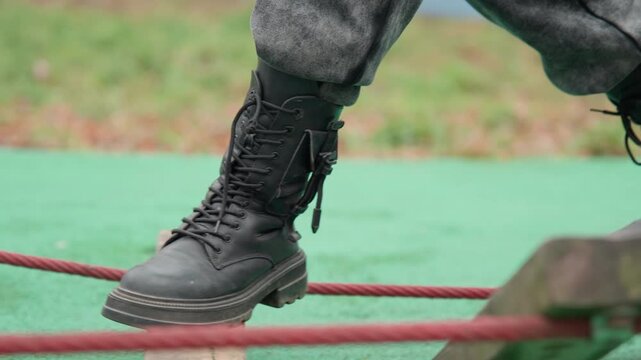 Combat boots training wooden rope obstacle, military recruit marching with disciplined steps across unstable planks, muddy tread and taut laces in gritty outdoor drill, closeup on sole and rhythm