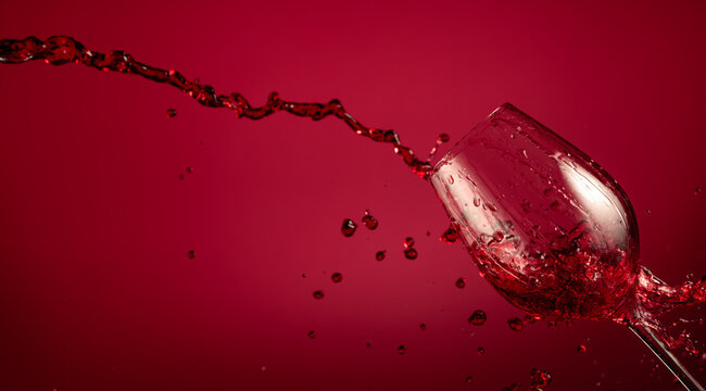 Glass and red wine splash on a red background.