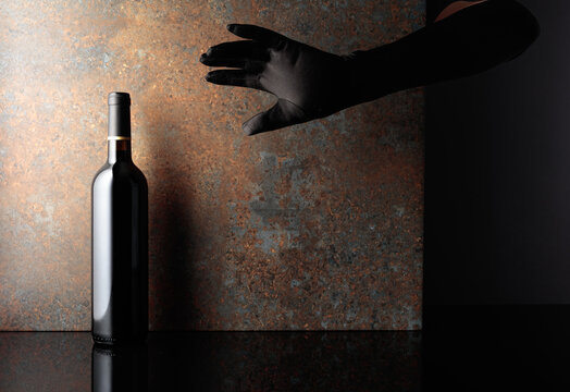 Woman hand in  glove reaches for a bottle of red wine.
