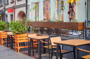 Obraz premium Cozy outdoor cafe with wooden tables and plants in the city. Summer terrace. Urban lifestyle.