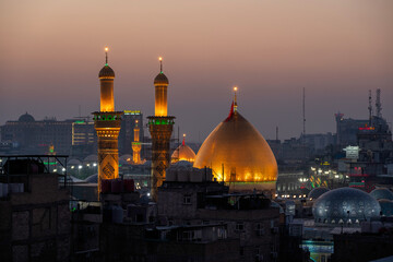 Fototapeta premium Karbala, Iraq - December 28, 2025: Golden dome and illuminated minarets of the Imam Hussain Shrine glowing at dusk in Karbala, Iraq