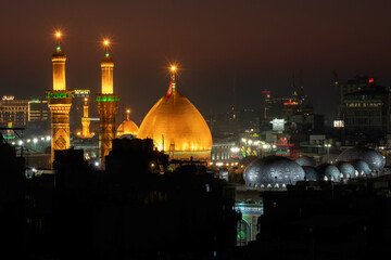 Fototapeta premium Karbala, Iraq - December 28, 2025: Golden dome and illuminated minarets of the Imam Hussain Shrine glowing at dusk in Karbala, Iraq