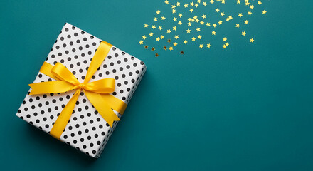 Obraz premium Polka dot gift box with yellow ribbon, scattered golden stars, representing celebration, surprise, and festive occasion, ideal for event promotion.
