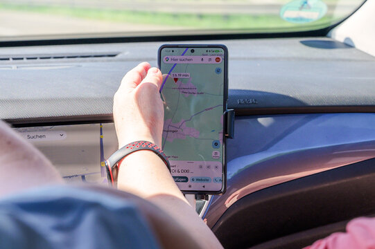 Augsburg, Germany &mdash; May 31 2026: A person wearing a fitness tracker touches a smartphone mounted on the car dashboard showing a Google Maps navigation screen near Untergermaringen