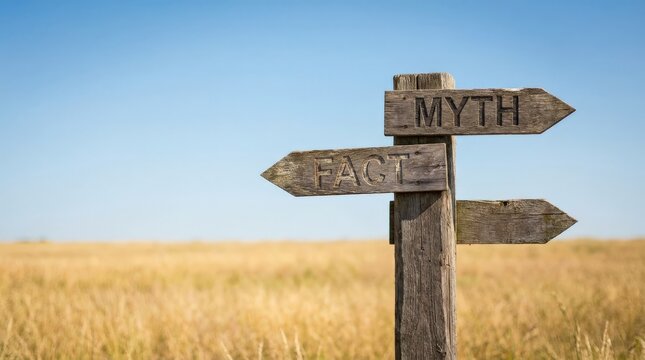 Wooden signpost with arrows pointing to fact and myth in a field with a blue sky background.