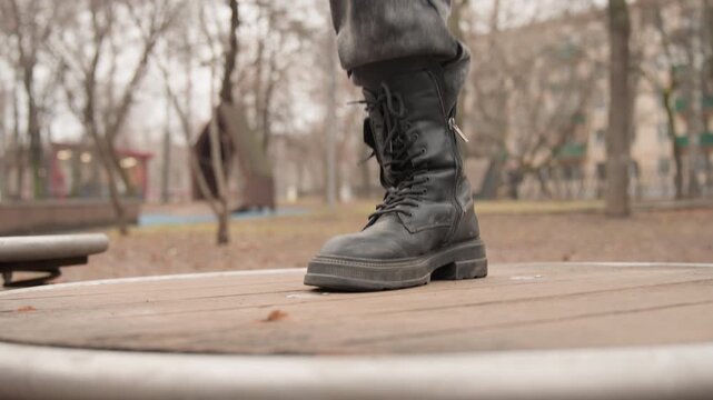 Worn black combat boots on carousel, closeup of sole and laces on wooden platform in autumn park, gritty weathered leather, subtle shift of weight and balance, blurred benches and bare trees in cold