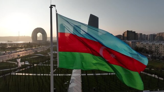 Azerbaijani flag waving in the wind with panoramic view of modern Baku skyline and city park at sunrise