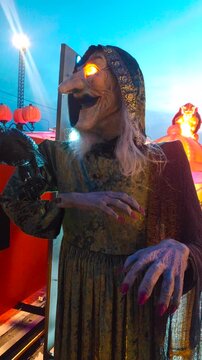 An animatronic old witch holding a raven on her arm, whose eyes glow at dusk on Halloween.
