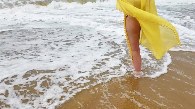 Woman legs in yellow pareo on beach with waves