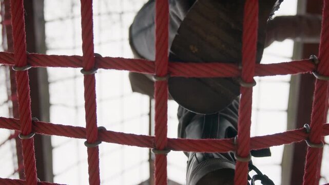 White woman stepping on red net closeup view of boots and laces through rope grid, soles pressing ropes, visible motion and tension, winter footwear, focus on grip and balance, abstract pattern