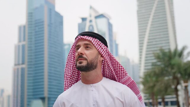 Man in Arab traditional clothing walking along Dubai Business Bay, surrounded by residential, commercial, and office towers and skyscrapers.