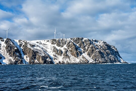 Winter scene of rocky coastline in Norway with wind turbines overlooking the sea and cloudy sky