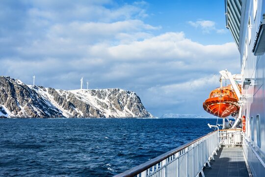 View from a ferry or cruise ship deck sailing in Norway to the snow covered mountains with wind turbines are visible in the distance