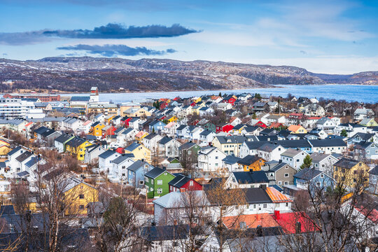 Colorful houses in Kirkenes in Norway near the water with mountains in the background during the day