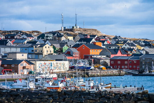 Fishing boats docked at the harbor in Vardo in Norway with colorful buildings  during a cloudy day