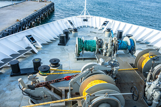 View from the deck of a ship showing winches and ropes with water in the background during the day