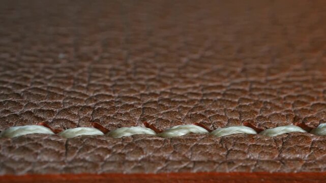 Extreme close up brown natural leather texture background with white seam, showing detailed grain, stitching of handmade product. Focus shifts along seam line. Brown natural leather seam macro detail