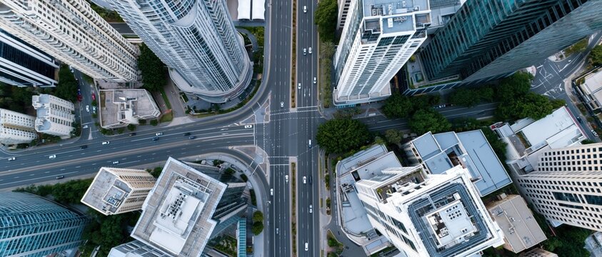 An overhead shot captures a vibrant urban intersection bustling with cars and modern skyscrapers, highlighting the dynamic movement and architectural beauty of the city.