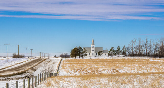 A historic rural church set against a vast winter prairie landscape, featuring distinctive white steeple, a typical Saskatchewan landmark representing the settlement history of Canadian prairies.
