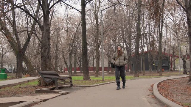 Man walking toward camera path morning commuter with backpack strides along winding park path flanked by leafless trees and empty benches, brisk pace, cool autumn air and introspective atmosphere