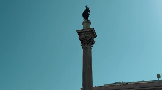 A bustling afternoon view of Piazza Colonna in Rome, Italy, featuring the historic Column of Marcus Aurelius surrounded by beautiful architecture and tourists enjoying a bright sunny day.

