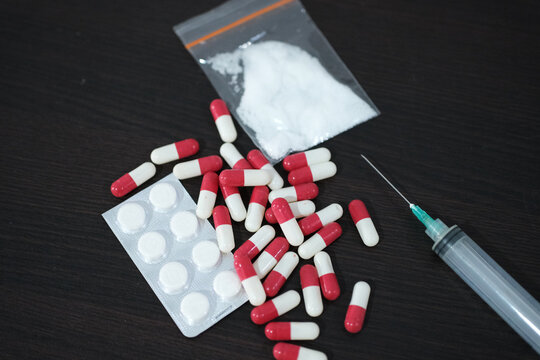 DRUGS, A syringe with pills, medication tablets, and a package of methamphetamine or heroin on a wooden table. The concept of drug trafficking and addiction.
