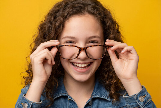 Happy curly girl putting on glasses smiling at camera on bright yellow background