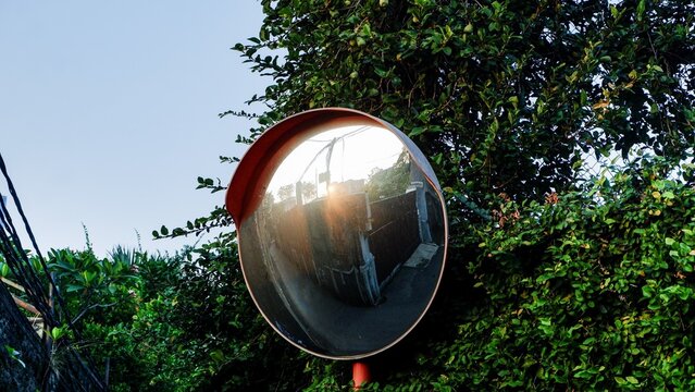 A detailed perspective on neighborhood accident prevention tools, highlighting a curved glass traffic mirror barrier installed by a roadside corner to help drivers navigate intersection views.