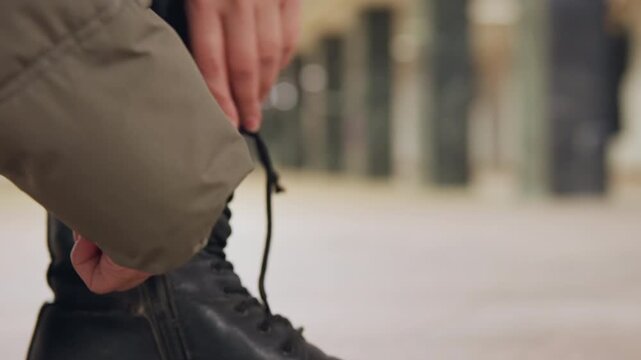 Focused individual secures dark shoes outside. Solo wanderer adjusts sturdy footwear on city street. Determined explorer ensuring black leather boots are tightly secured on cracked pavement