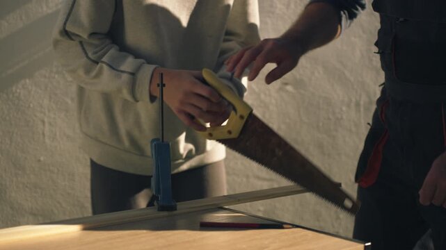 Caring father teach young son how to saw wood, sharing valuable carpentry skills and knowledge during sunny day of diy work, fostering strong bond and creating lasting memories