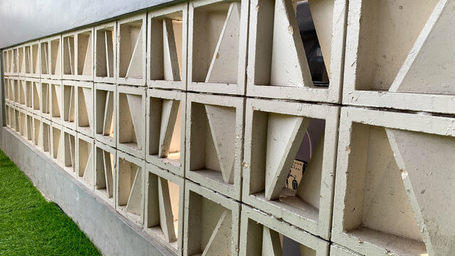 Close-up perspective of a traditional concrete roster (ventilation blocks) wall with a geometric triangle pattern. Classic tropical architectural design for air circulation and natural light.