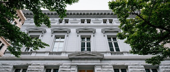 Fototapeta premium This image features a grand, elegant building facade framed beautifully by lush green trees, symbolizing a harmonious blend of architecture and nature in an urban setting.
