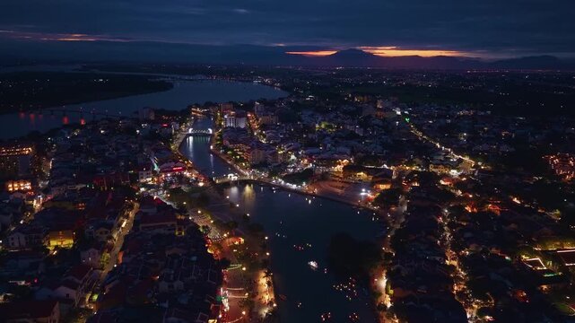 Aerial view of river with lit boats and bustling riverside market in historic town Hoi An at night, Vietnam travel.