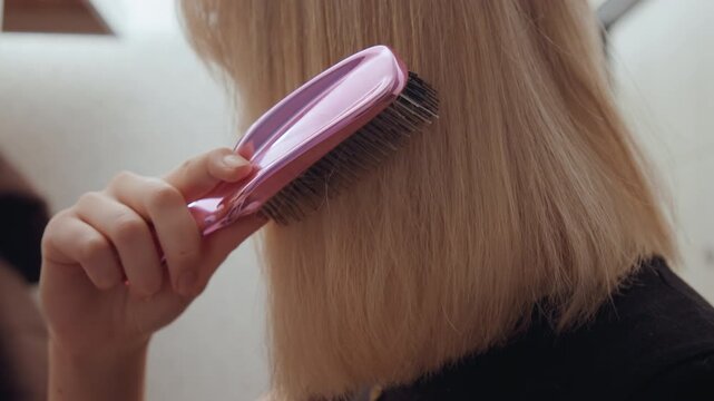 White woman smoothing blonde hair with brush, intimate closeup of bristles gliding through strands, visible hair texture and shine, cropped bob ends and soft lighting, focused finishing touch